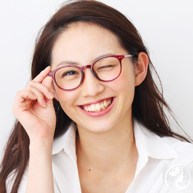 眼鏡をかけた知的な女性がウィンクしながら笑顔を見せる｜小顔矯正で若々しく明るい印象に