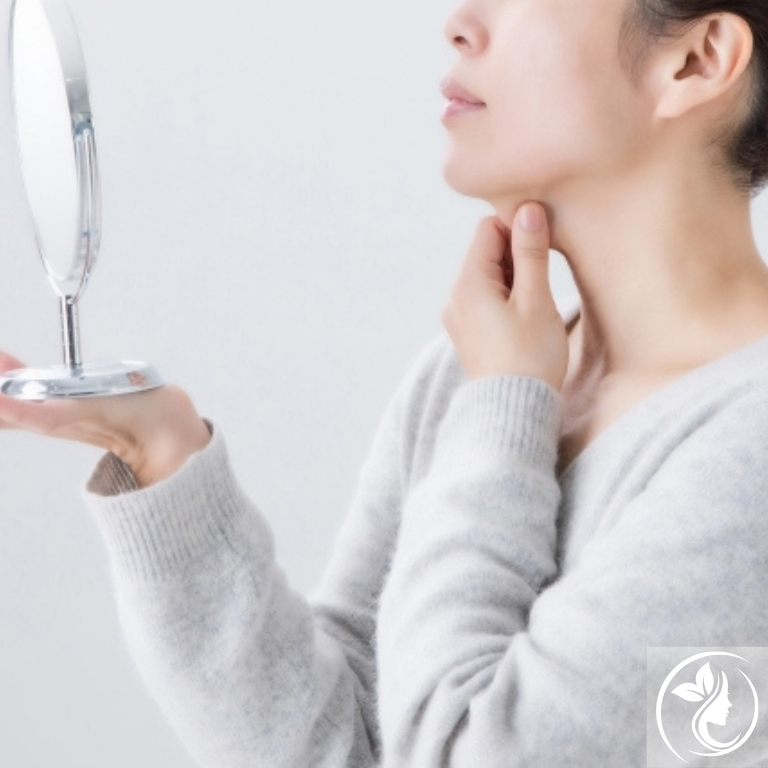 鏡でフェイスラインを確認する女性。たるみや二重あごが気になり始めた40代の小顔ケアや若見え美容習慣に注目｜足立区梅島AloHa